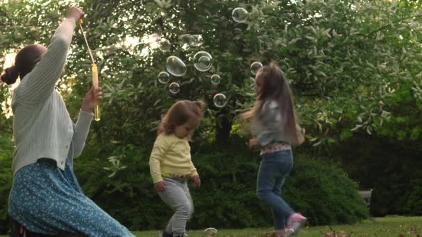 Happy family mother, two Three little siblings kids are blowing soap bubbles and enjoying summer holidays in garden or park . Smiling parents children are spending leisure time together evening sunset — Stok video