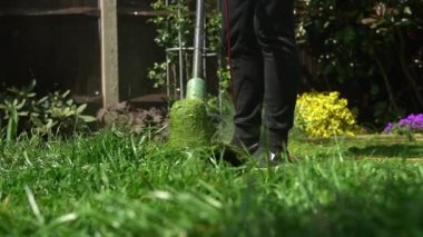 Çim biçme makinesi çim biçiyor. Çim biçme makinesinden çıkan küçük yeşil çim biçme makineleri peyzajcılar tarafından itilip kakılıyor. Ağır çekim. Bahçıvan adam bahçe bahçesinde çim biçme makinesiyle çalışıyor. Aile, iş.