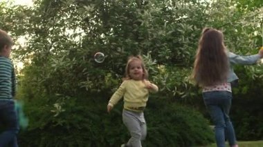 Mutlu bir aile annesi, iki küçük kardeş çocuk sabun köpüğü üflüyor ve yaz tatillerinin tadını çıkarıyorlar. Gülümseyen ebeveynler çocuklar akşam günbatımında birlikte vakit geçiriyorlar.