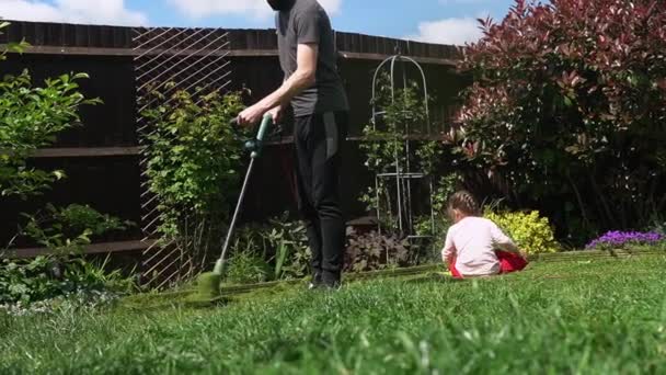 Lawn mower cutting grass. Small Green grass cuttings fly out of lawnmower pushed around by landscaper. Slow motion. Gardener Man working with mower machine in Garden Outside Sunny Day.Family, Work — стоковое видео