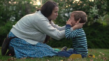 child is crying in park in arms of mom. Mommy soothes baby boy. family mother and child with tears in their eyes. emotionally. loving young mother hugs and soothes her little Son in Park. Motherhood.