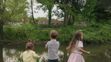 Mutlu bir aile. Üç çocuk göl kenarında koşuyor, balığa gidiyor. Park konseptindeki insanlar. Oğlan ve kız kardeşler neşeli bir yaz geçiriyorlar. Küçük çocuk gülümseyen çocuk koşuyor rüya gibi bir yaşam tarzı.