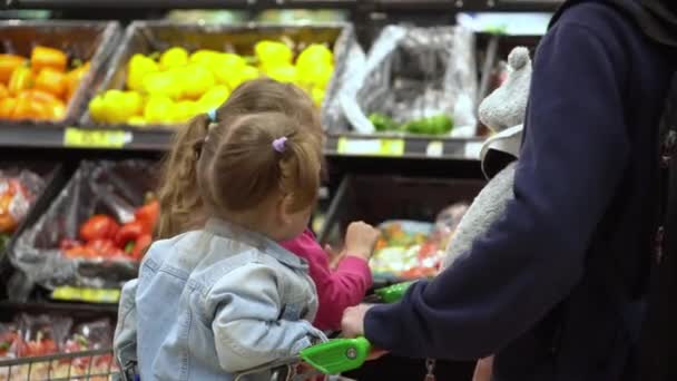 购物清单上的粮食危机概念 父亲和两个女儿在超市 孩子们坐在推车上 孩子们和爸爸一起吃新鲜蔬菜和水果 健康饮食生活方式 — 图库视频影像