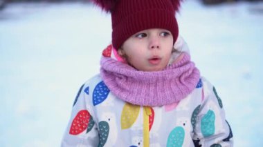 Close up Portrait Little Child Pretty Girl Kid Smiling Looking at Camera posing in red hat coughing Snow Park Outdoor. Winter time, happiness concept. Snowing Cold frosty weather. Carefree childhood.