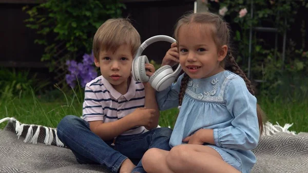 两个快乐兄弟男孩的女孩在花园外面的耳机里听音乐 儿童与技术 哥哥和姐姐 热爱音乐 喜欢做梦 — 图库照片