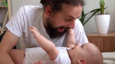 Uzun saçlı otantik sakallı genç baba ve yeni doğmuş bebek yatakta gülümsüyor. Baba, bebek bebekle yatıyor. Çocuklar, Ebeveynlik, Çocukluk, Hayat, Aşk, Babalık, Aile Kavramı