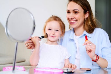 Genç mutlu anne anaokulu kızıyla oynuyor ve makyaj yapıyor.