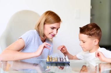 Beyaz anne ve küçük oğlu evde satranç oynuyorlar.