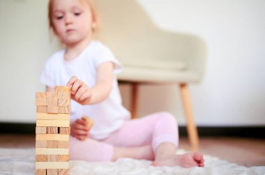 Little cute preschool girl playing jenga on the floor at home and collecting wooden cubes