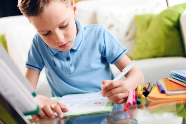 Pensant enfant ennuyé, petit garçon écrivant soigneusement assis au bureau et faisant des devoirs Photos De Stock Libres De Droits