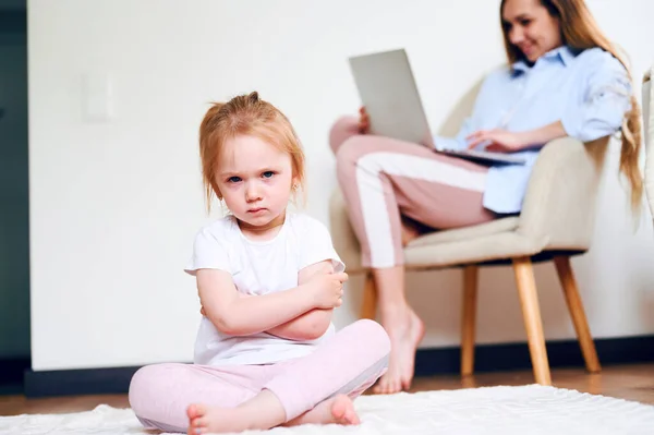 Niña molesta sentada sola mientras la madre usa el portátil. Madre no tiene tiempo para su hija. — Foto de Stock
