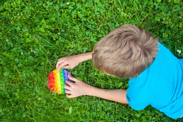 丸い虹で遊んでいる男の子はそれをおもちゃにポップ 新しいフィジェットトレンディーなおもちゃ ストレス対策のおもちゃ シンプルなディンプル — ストック写真