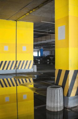 Binanın altına park etmek (otopark altı). Beton kolonlar. Asfalttaki su birikintileri park yerinin duvarlarını ve tavanını yansıtıyor..