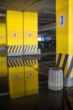 Binanın altına park etmek (otopark altı). Beton kolonlar. Asfalttaki su birikintileri park yerinin duvarlarını ve tavanını yansıtıyor..