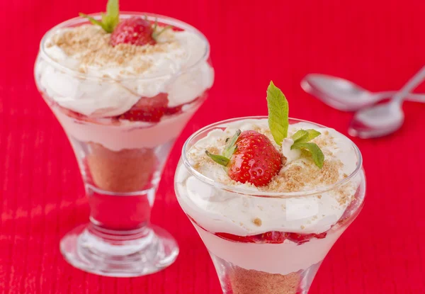 Two strawberry and cream desserts on red background