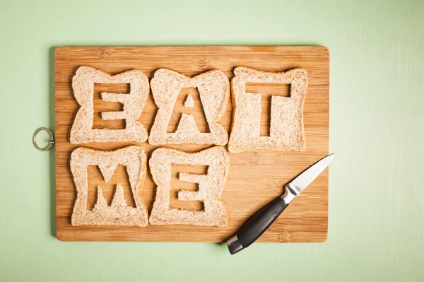 Eat me text carved out of brown bread slices