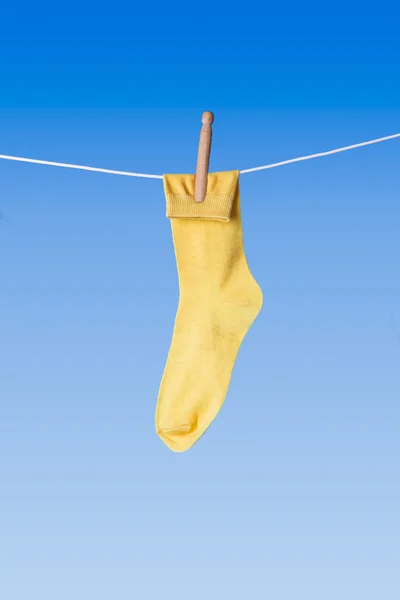 Calcetín amarillo en la línea de lavado contra fondo azul Fotos De Stock Sin Royalties Gratis