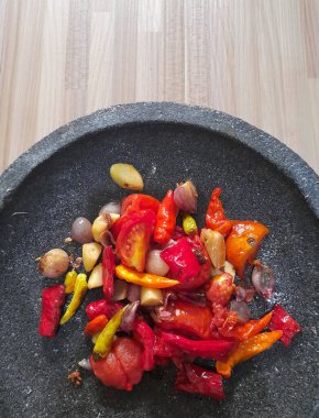 Çili soslu taş kâse, ahşap arka planda biber ve sarımsak.