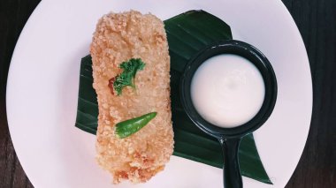 Risoles mayonez, mayonez, sosis, muz yaprağı ve beyaz tabakta servis edilen ahşap bir masa. Yaklaş, yumuşak odaklan.