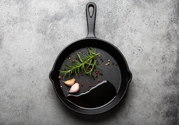 Black cast iron frying pan with rosemary, garlic, pepper, oil — Stock Photo, Image