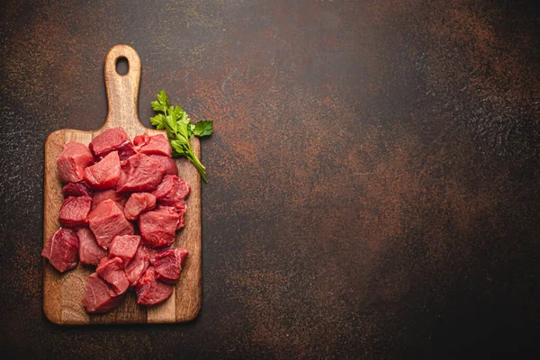 Nötkött rå kött kuber för stuvning på trä skärbräda kopia utrymme — Stockfoto