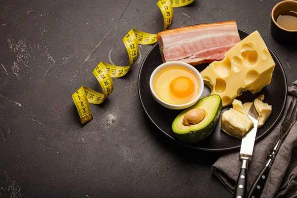 Foods for keto diet on black plate, measure tape on dark background