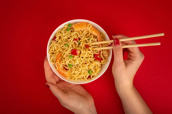 Female hands with bowl of shrimp noodles on red background — Stock Photo, Image