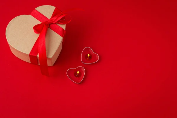 Gift boxe in heart shape with bow and two candles on red background, Saint Valentine Day — Stock Photo, Image