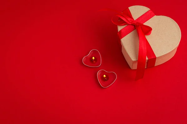 Gift boxe in heart shape with bow and two candles on red background, Saint Valentine Day — Stock Photo, Image