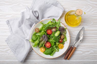 Vegetables healthy salad with red yellow cherry tomatoes and green salad leafs on white rustic ceramic plate