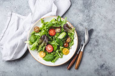 Vegetables healthy salad with red and yellow cherry tomatoes, pepper and green salad leafs on white rustic ceramic plate