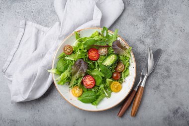 Vegetables healthy salad with red and yellow cherry tomatoes, pepper and green salad leafs on white rustic ceramic plate