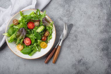 Vegetables healthy salad with red and yellow cherry tomatoes, pepper and green salad leafs on white rustic ceramic plate