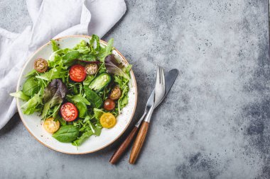 Vegetables healthy salad with red and yellow cherry tomatoes, pepper and green salad leafs on white rustic ceramic plate