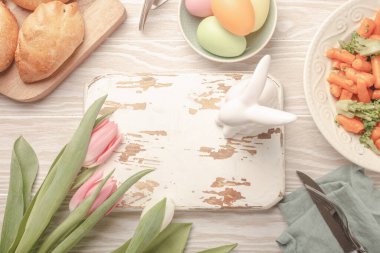 White empty wooden cutting board and Easter food on kitchen table