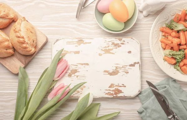 White empty wooden cutting board and Easter food on kitchen table — Stock Photo, Image