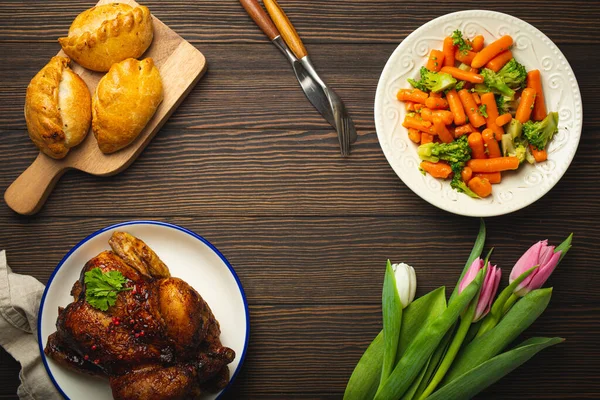 Easter food on dark rustic table: pastel colored eggs, roasted chicken, vegetables, buns — Stock Photo, Image