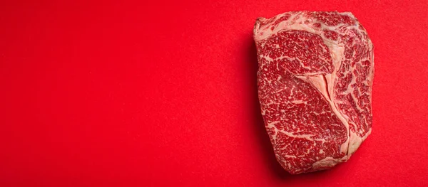 Råkött nötkött prime cut steak Ribeye på ren röd bakgrund uppifrån, nötkött koncept banner minimalism — Stockfoto