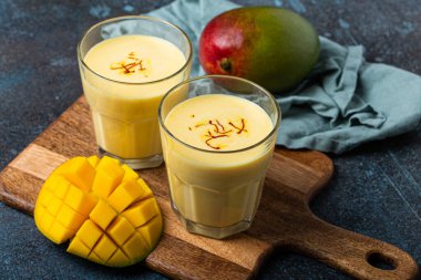 Yukardan taze kesilmiş manfo ile kırsal beton masada iki bardakta mango lassi iç.
