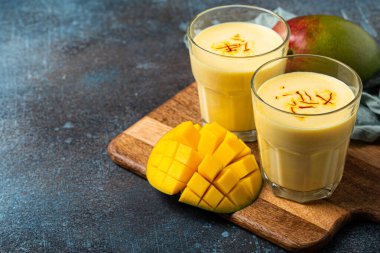 Yukardan taze kesilmiş manfo ile kırsal beton masada iki bardakta mango lassi iç.