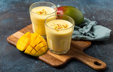 Yukardan taze kesilmiş manfo ile kırsal beton masada iki bardakta mango lassi iç.
