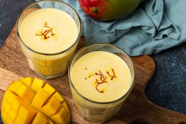 Yukardan taze kesilmiş manfo ile kırsal beton masada iki bardakta mango lassi iç.