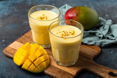 Yukardan taze kesilmiş manfo ile kırsal beton masada iki bardakta mango lassi iç.