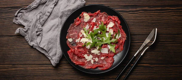 Koud vlees voorgerecht Rundvlees carpaccio met parmezaanse kaas en arugula op zwarte plaat — Stockfoto