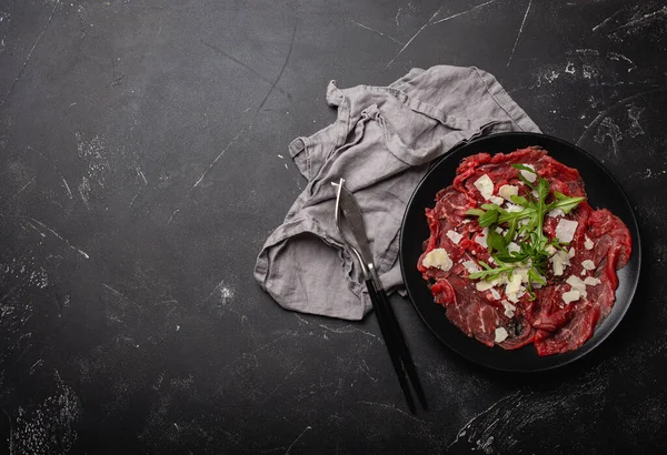 Antipasto di carne fredda Carpaccio di manzo con parmigiano e rucola su piatto nero — Foto Stock