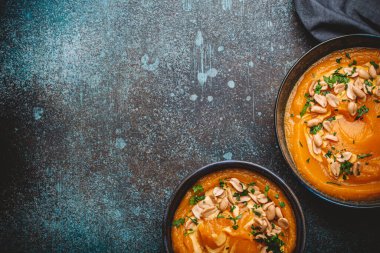 Koyu taştan arka planda yer fıstıklarıyla süslenmiş, yukarıdan süslenmiş balkabağı kremalı bir seramik kâse. Sonbahar sıcacık akşam yemeği konsepti, metin için boşluk