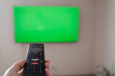 Rusya, Barnaul, 25 Ekim 2021: Uzaktan kumandayla TV programında sörf yapmak. Genç kız oturma odasında ya da yatak odasında televizyon izliyor. kopyalama alanı. Kız televizyon izliyor. Seçili odak