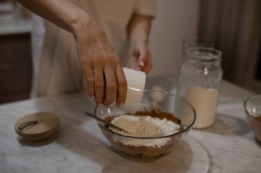 The girl pours the flour into the dough from the glass. The girl prepares the dough for the cake. Selectiv focus