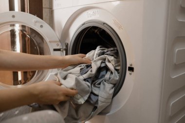 The girl loads the washing machine with dirty laundry.