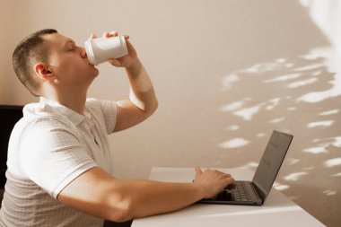A young man works from home and drinks coffee. A man studies and drinks coffee at home.